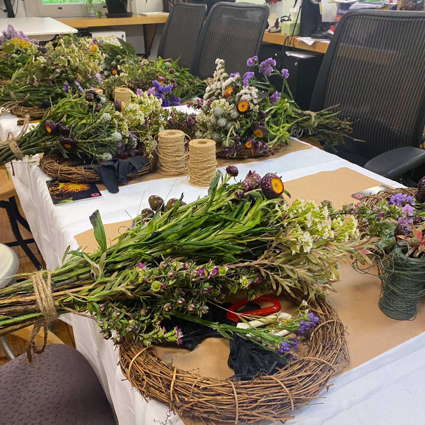Assorted floral arrangements and a wreath on a table with a white cloth.