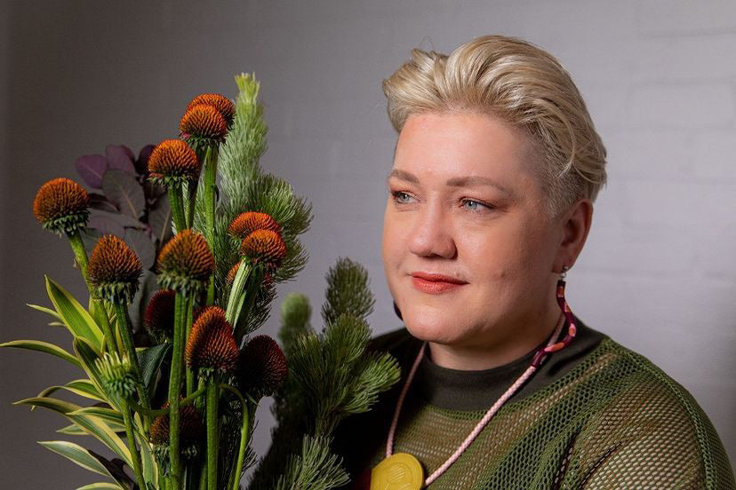 A close up portrait of Suz from Bold Botanicals holding a bouquet of green and brown flowers