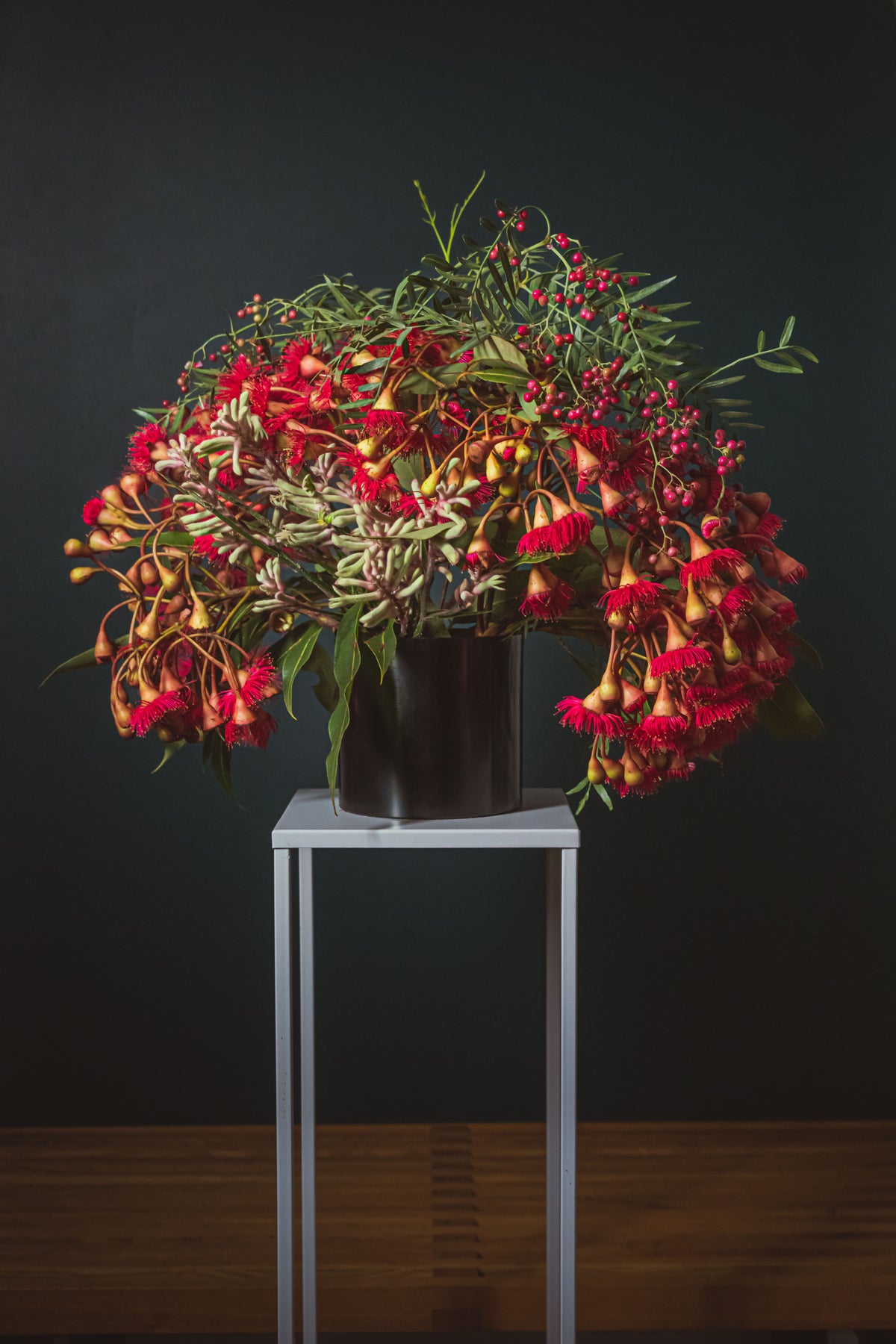 A festive flower arrangement of yellow and red flowers in a black pot sitting on a tall, white table