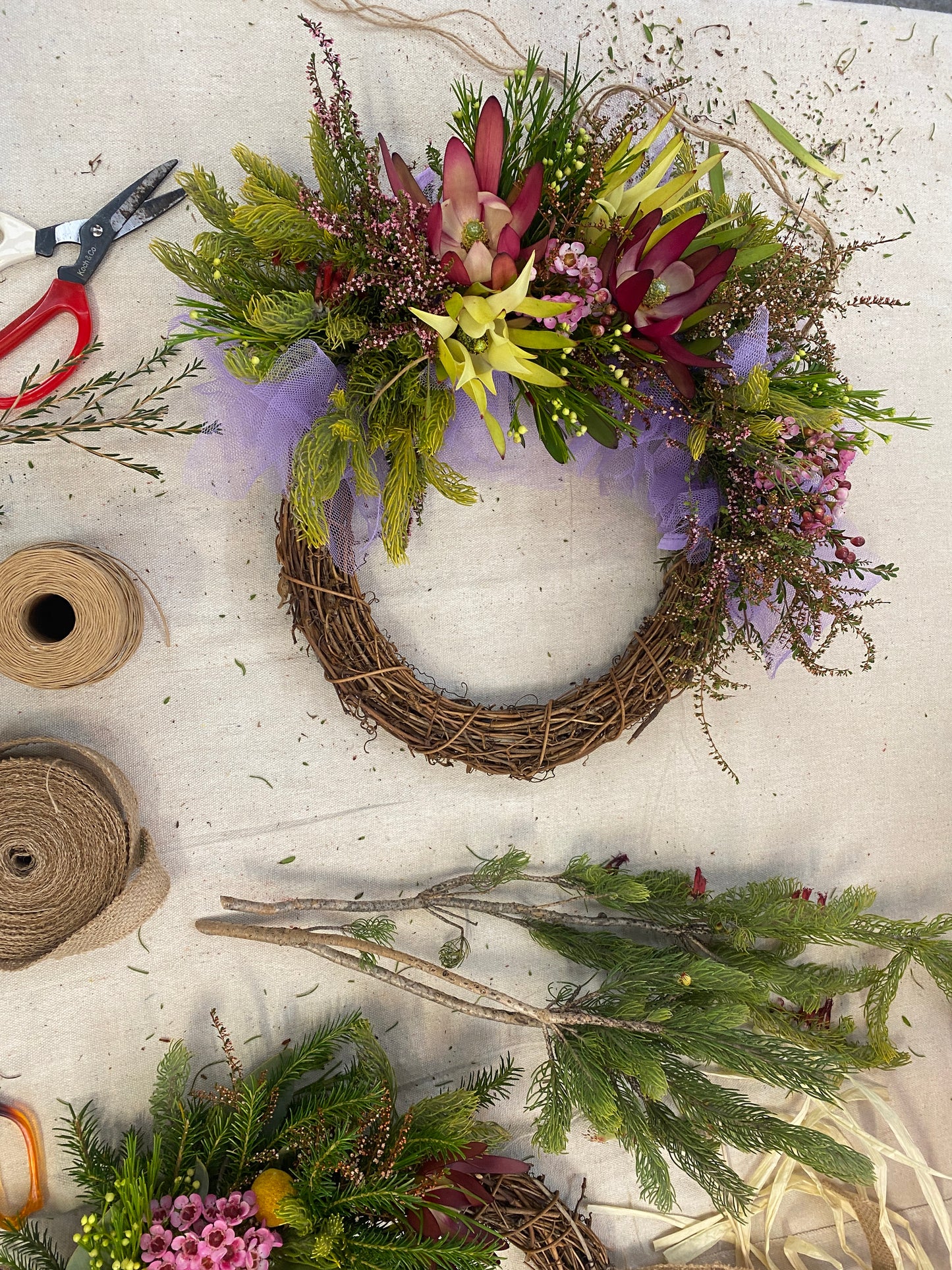 A grapevine Christmas wreath decorated with native Australian flowers displayed on a table with accessories placed around it