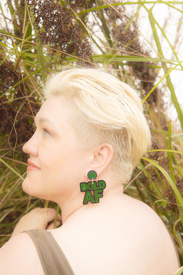 Doodad and Fandango designed earrings on a model depicting the words BOLD AF in green