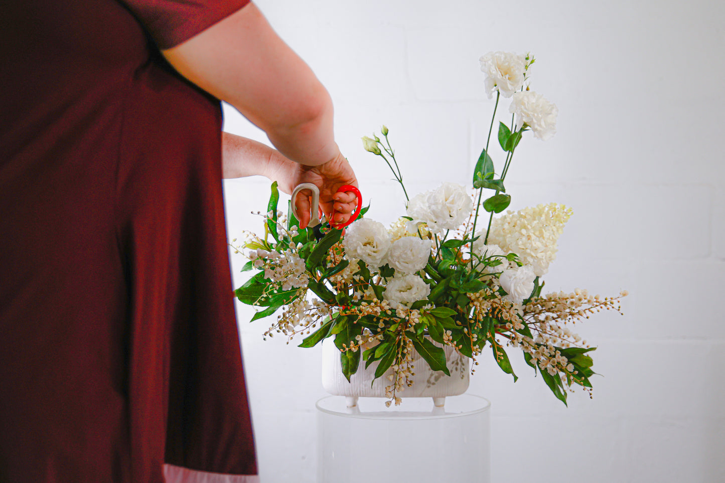 Floral arrangement of white flowers being pruned by Suz from Bold Botanicals in a burgundy dress