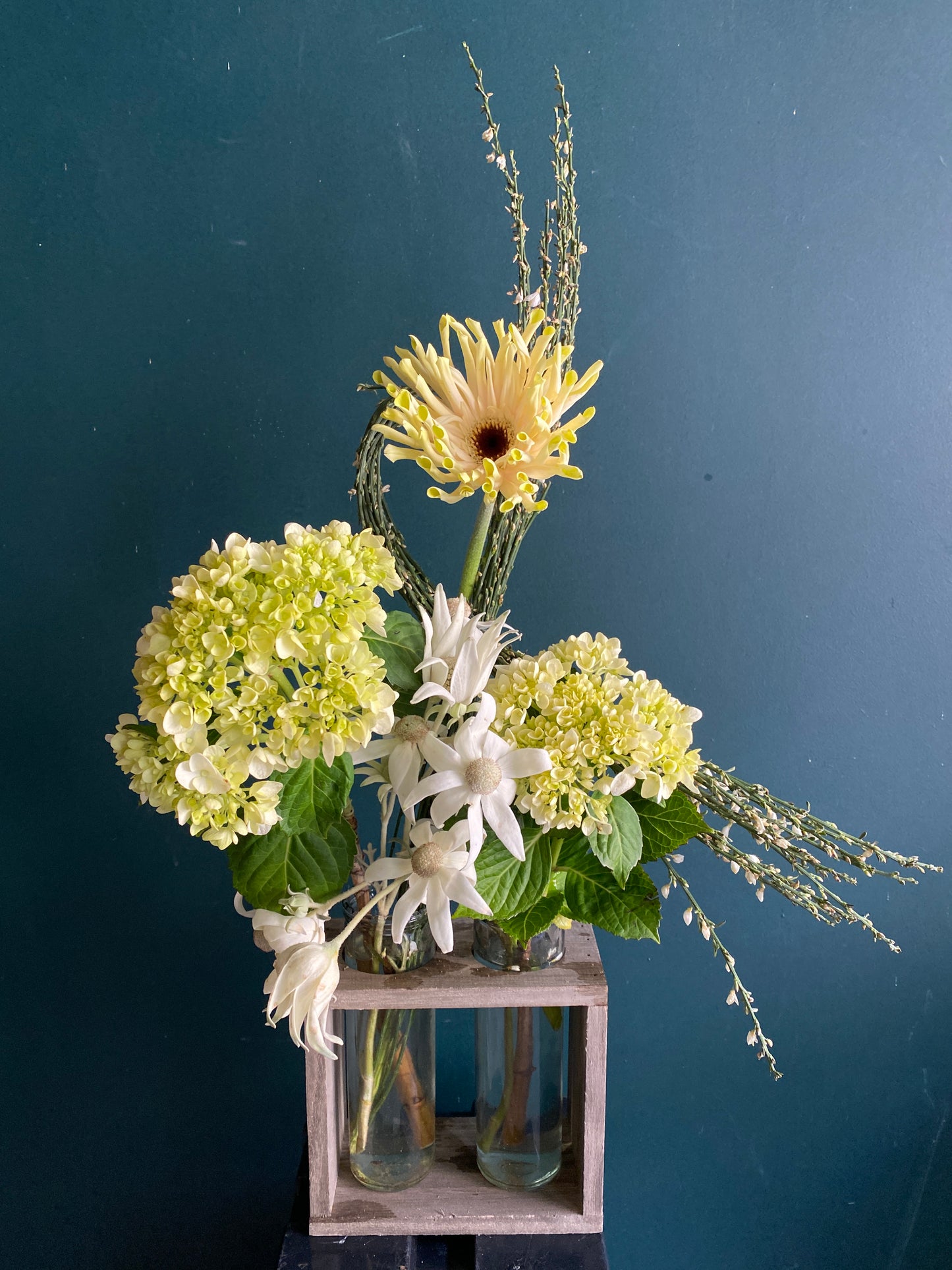 An arrangement of yellow and white flowers in glass tubes within a small, wooden box