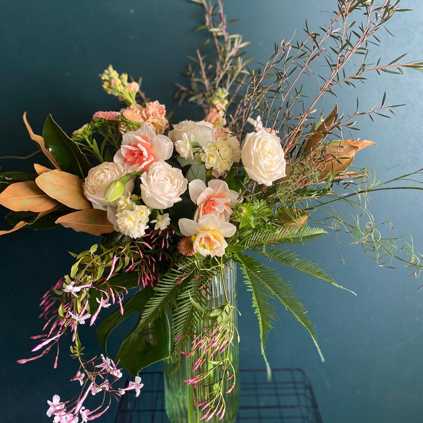 An arrangement of seasonal white, yellow and pink flowers in a tall, rippled glass vase