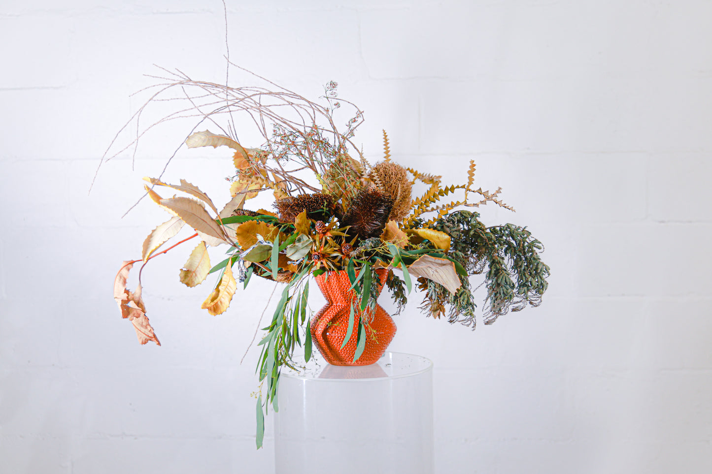 An arrangement of Australian native flowers in an orange vase sitting atop a glass table