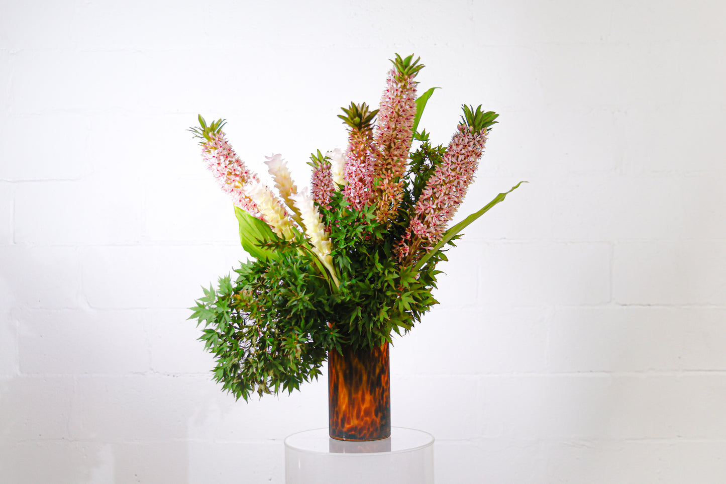 An arrangement of pink, bushy flowers with green foliage in a dark brown glass vase