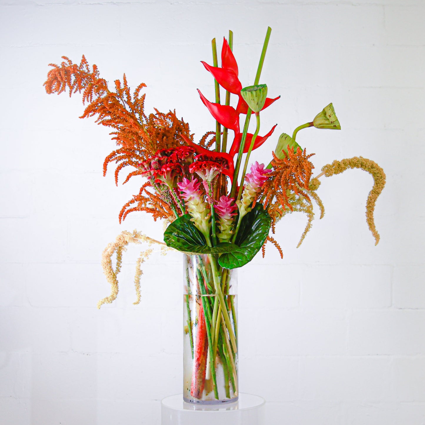 A stunning tall tropical corporate arrangement with lotus pods, heliconia and amaranthus