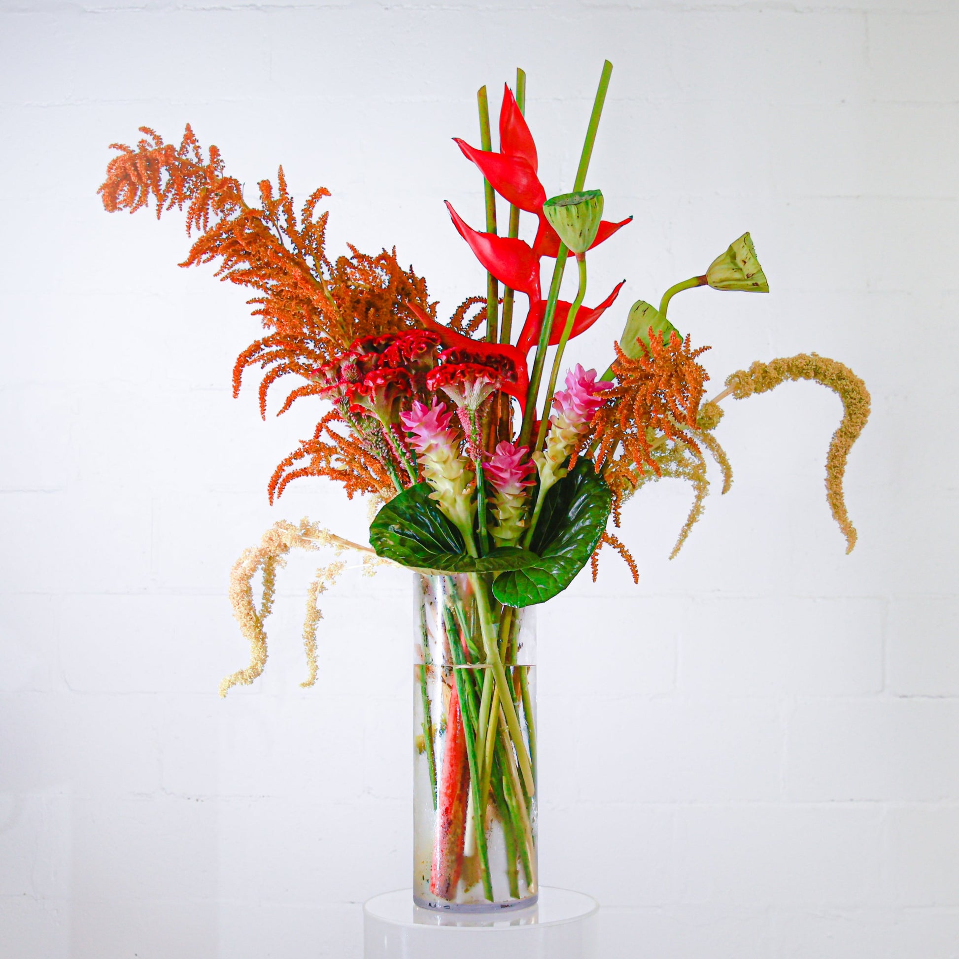 A stunning tall tropical corporate arrangement with lotus pods, heliconia and amaranthus