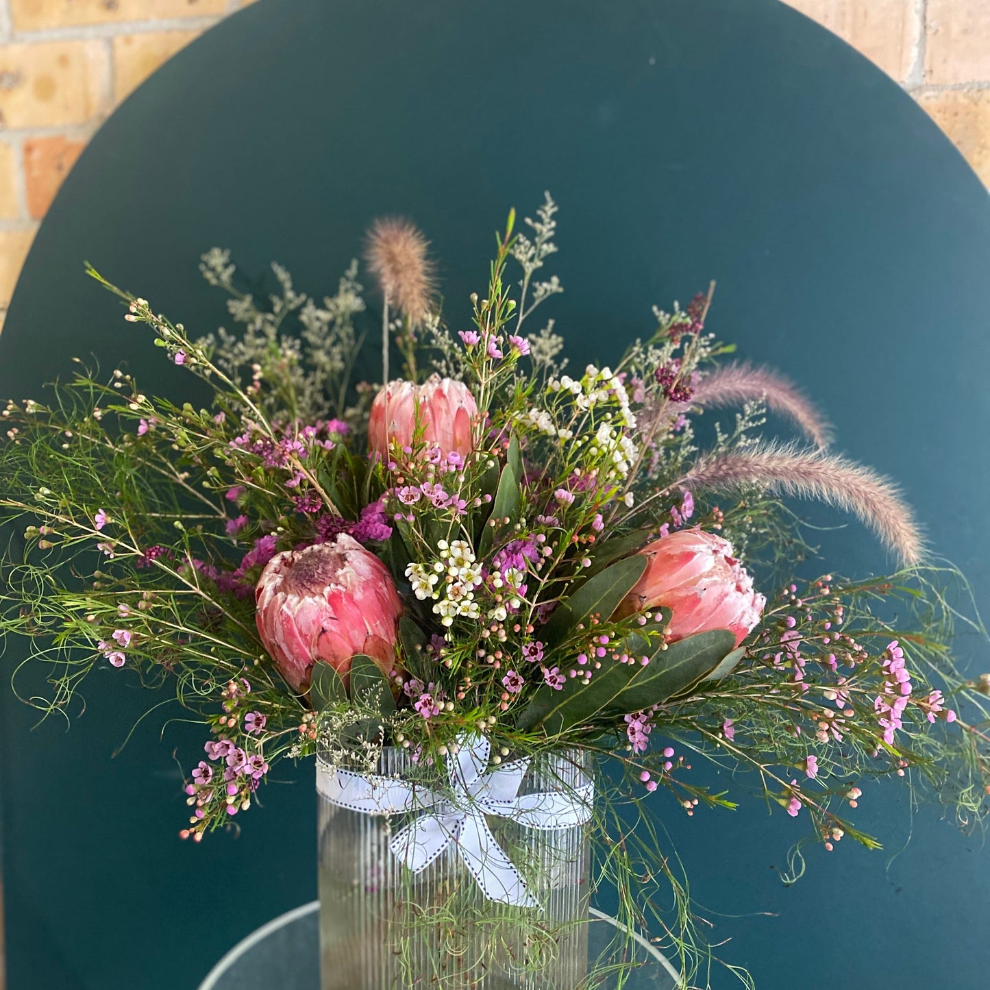 A Large sized Bold Betty Australian Natives flower arrangement being sent as Sympathy in a ribbed vase with ribbon