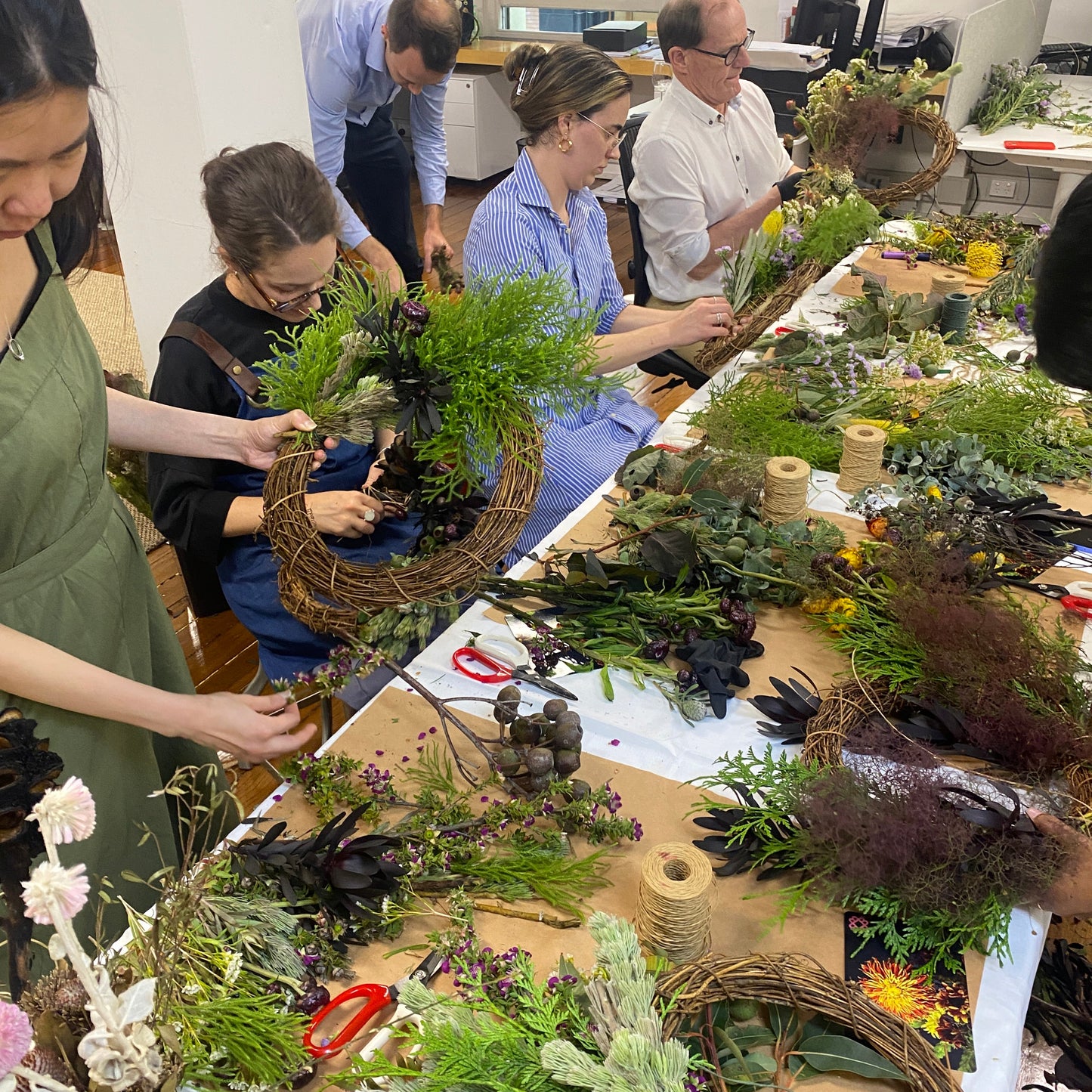 Group of people working on floral arrangements at a table.