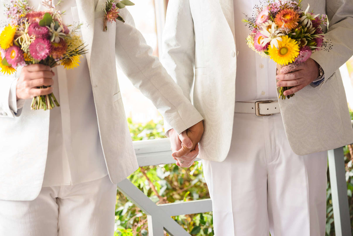 Two men holding hands at their wedding, each holding small, colourful, native flower bouquets made by Bold Botanicals