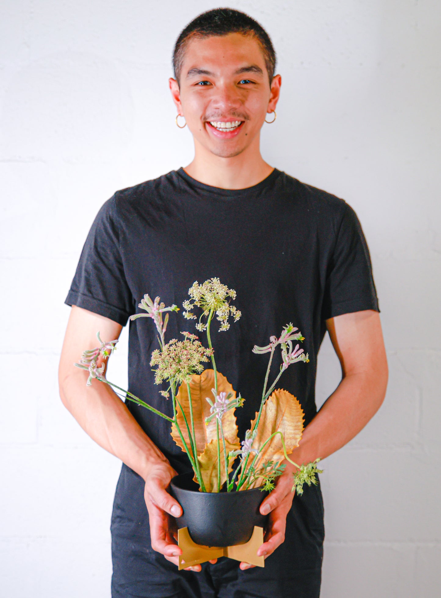 Young man wearing black shirt and pants holding a pot of flowers