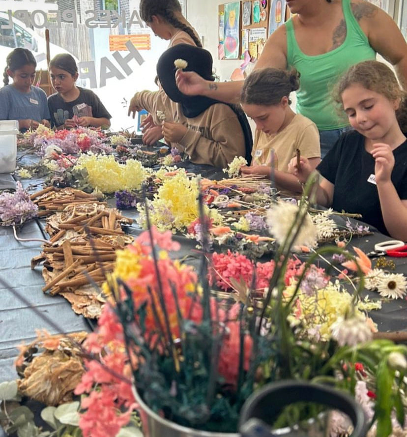 A table with flowers and accessories spread out with children making flower crowns at a Bold Botanicals workshop