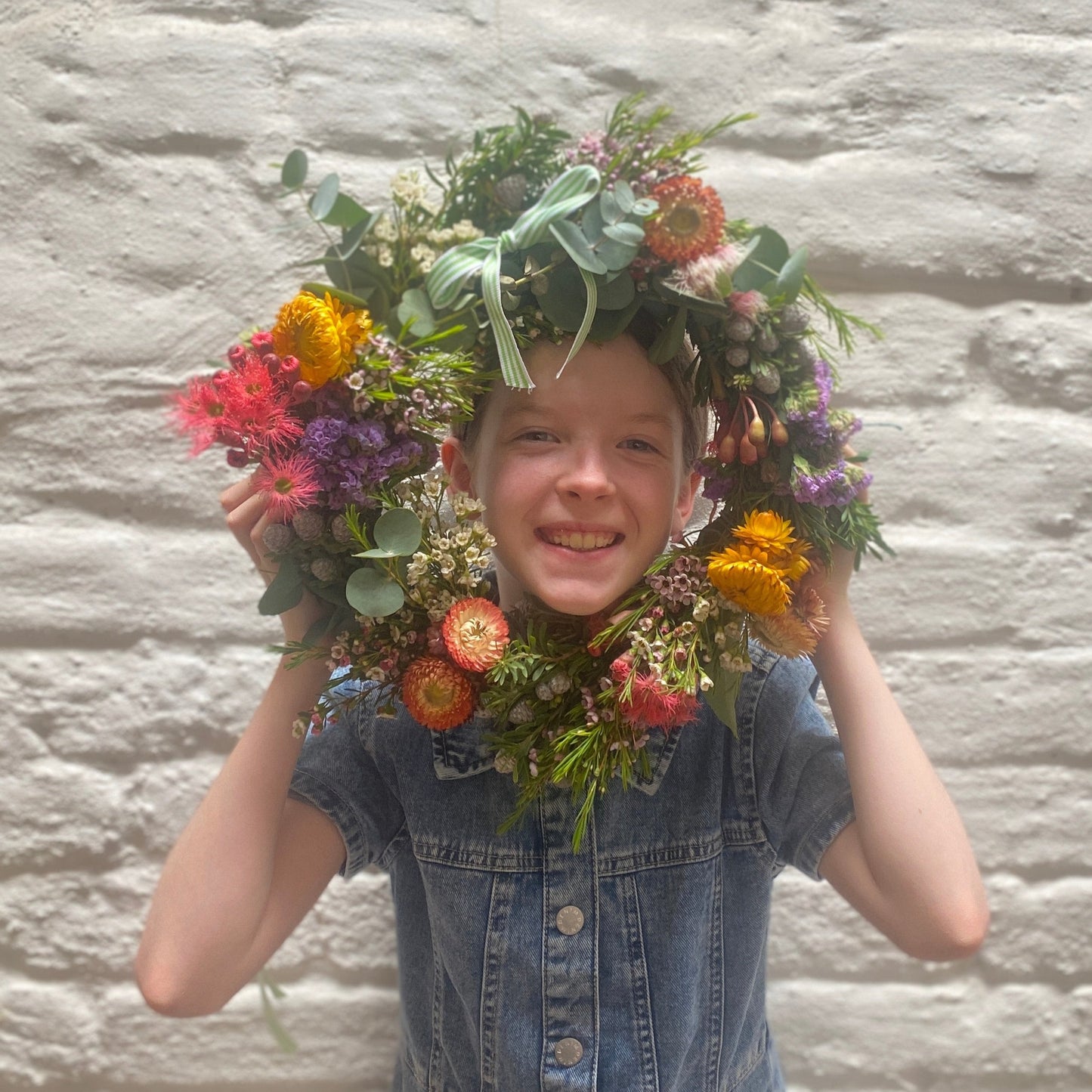 A happy girl holding her completed Christmas wreath made with Australian native flowers around her face