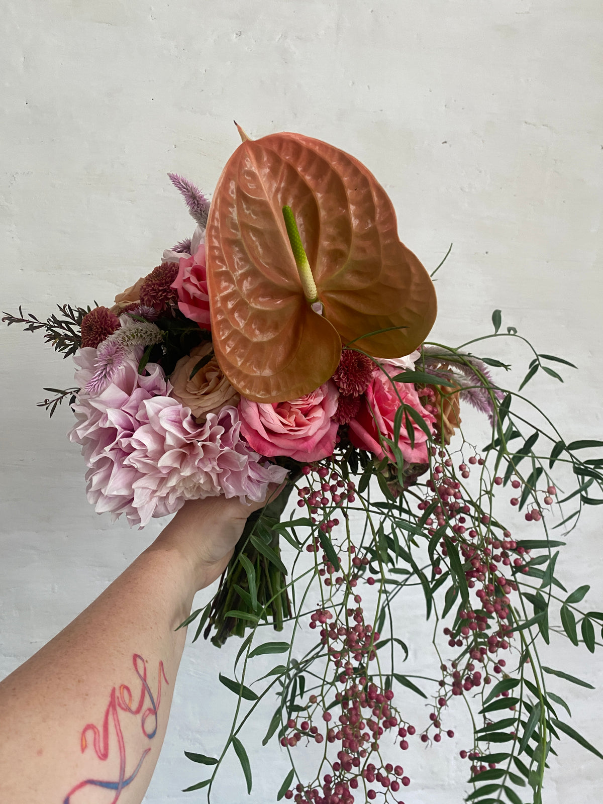 Bouquet of flowers held by a person with a tattoo on a light gray background