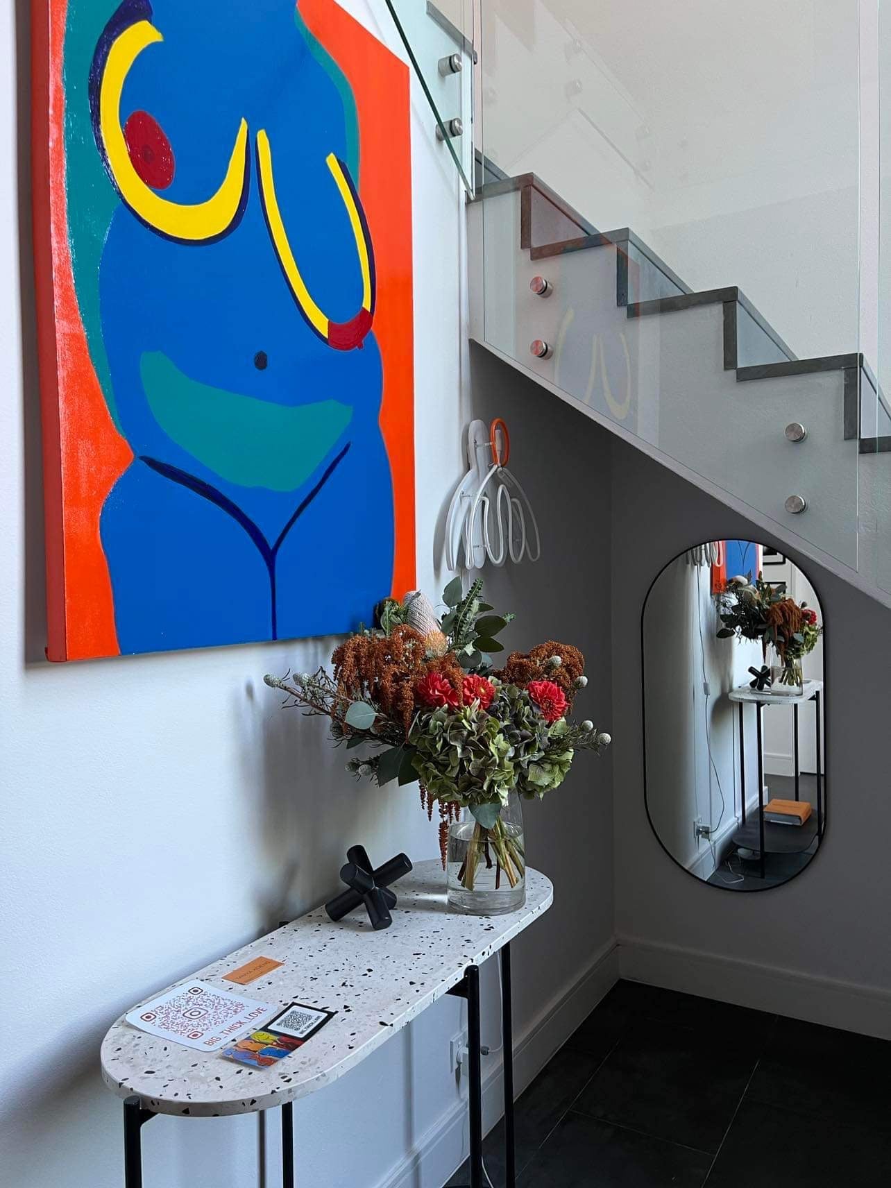 Medium seasonal flower arrangement at entry to house for sale. Bold colourful art above to bring out the orange flowers.