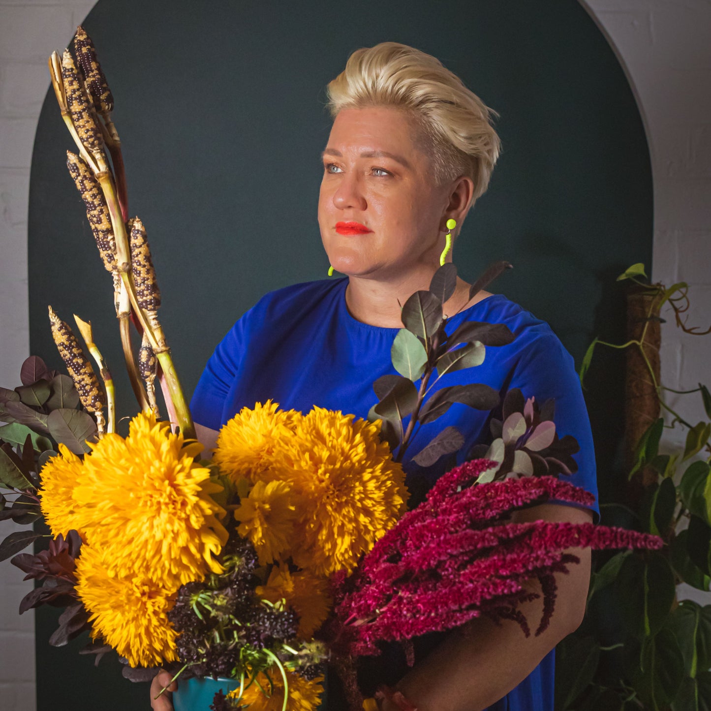 Florist Suzanne stands with a stunning Bold Experience arrangement in a pot, featuring teddy bear sunflowers and other exotic flowers.