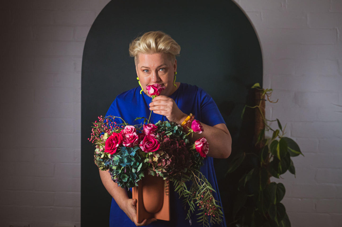 Suzanne our florist with a large vase of roses and hydrangea, smelling the rose