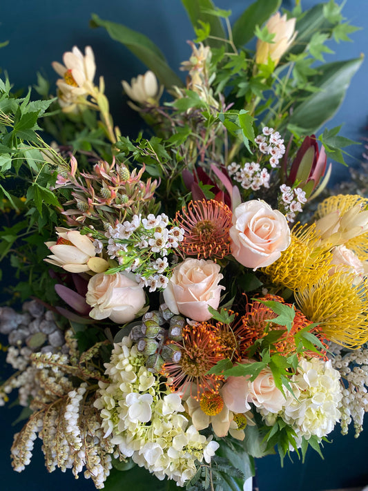 seasonal flowers in soft pink and peach, yellow, orange and greenery against a deep green background