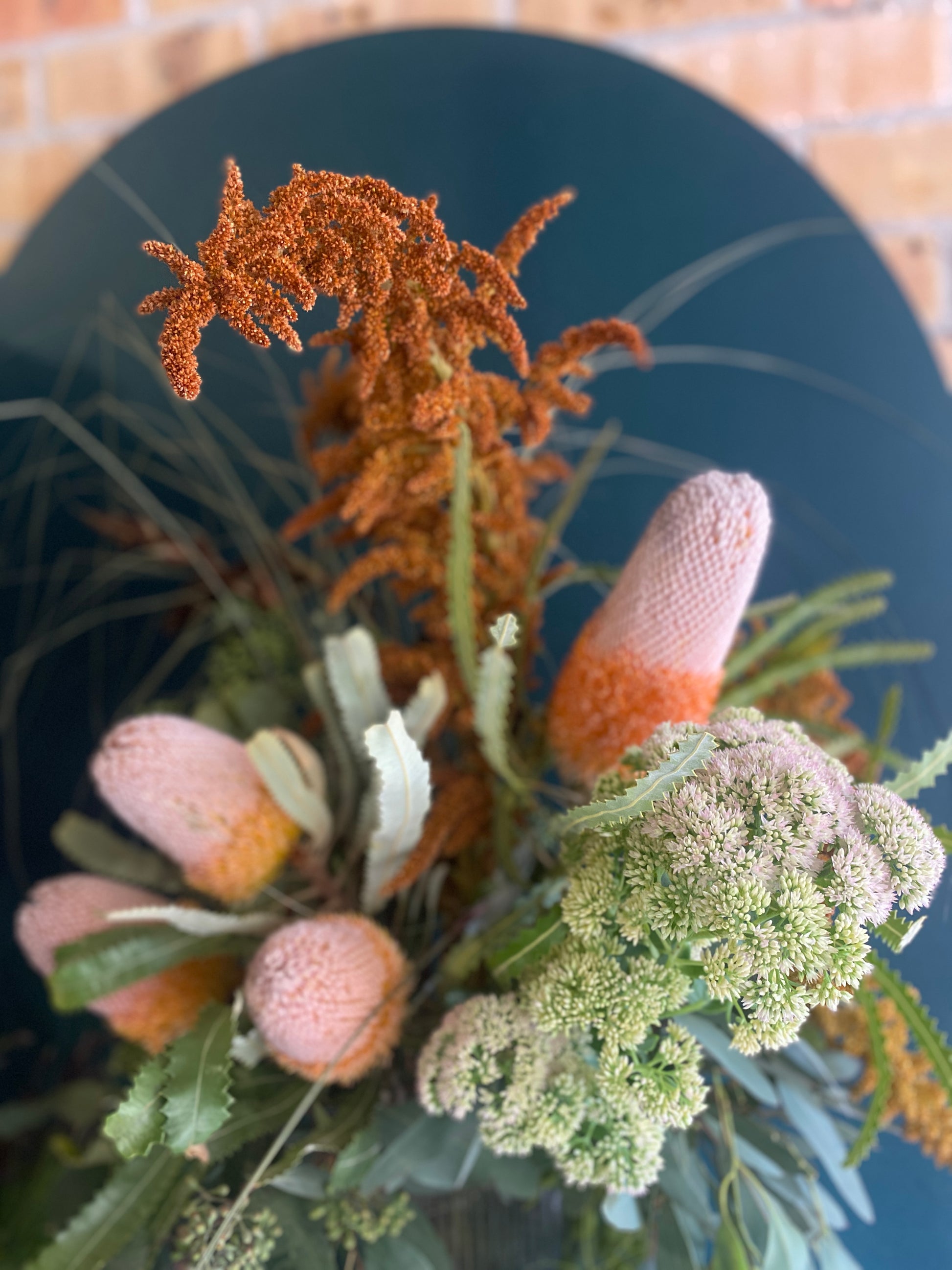 Decorative arrangement of flowers and plants on a dark surface with a brick wall background.