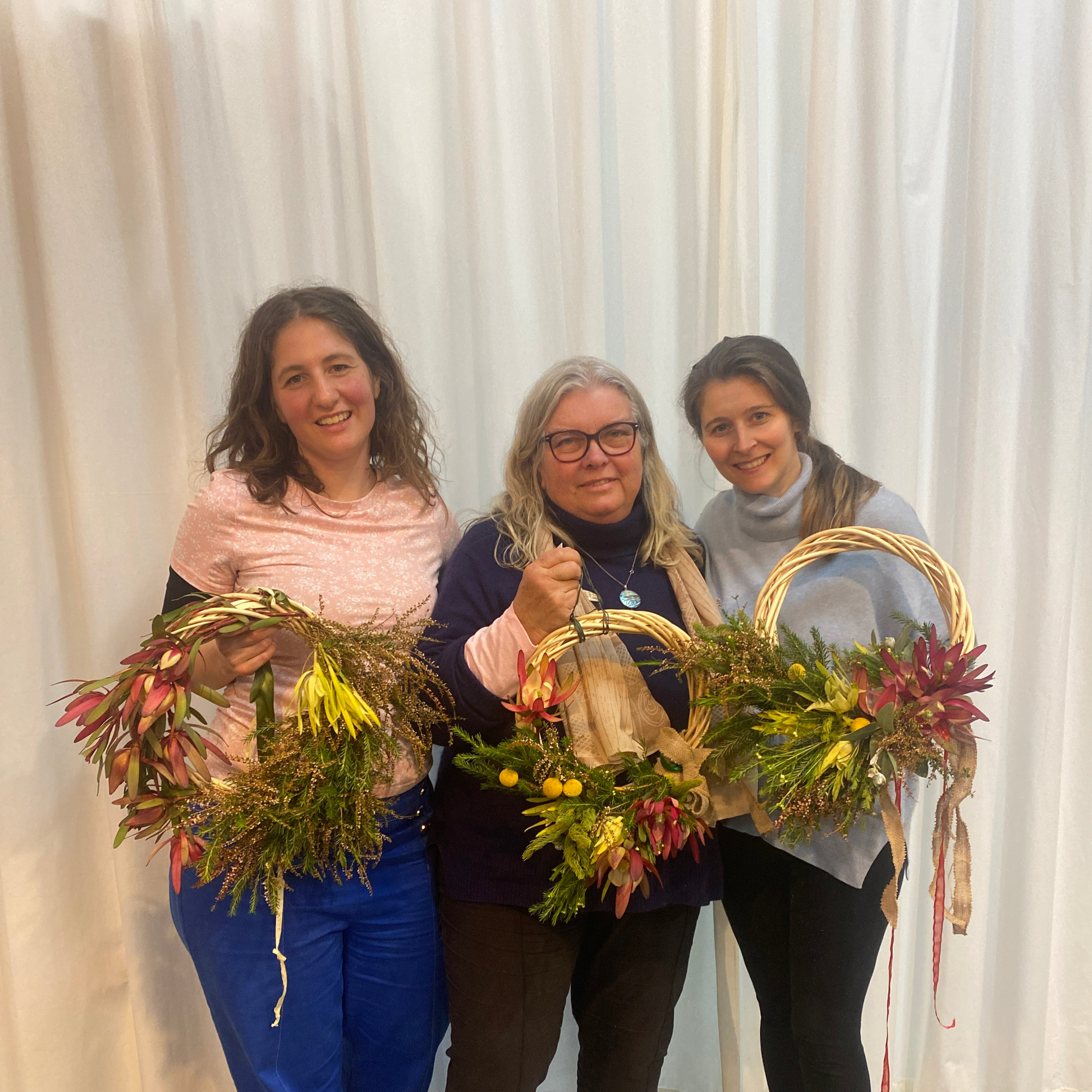 Three smiling women holding up Christmas Wreaths made in a Bold Botanicals workshop