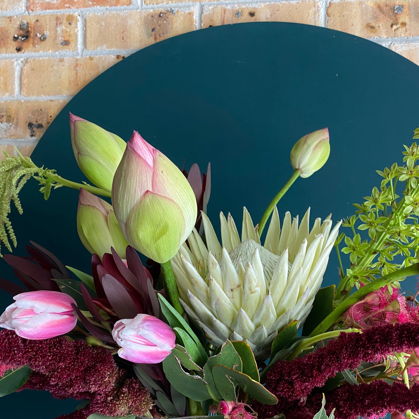 A bold flower design in a vase featuring lotus flowers, pink flowering gum and red amaranthus