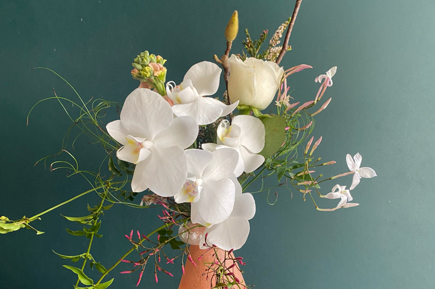 White and pink flowers arranged with green foliage in a small apricot coloured vase