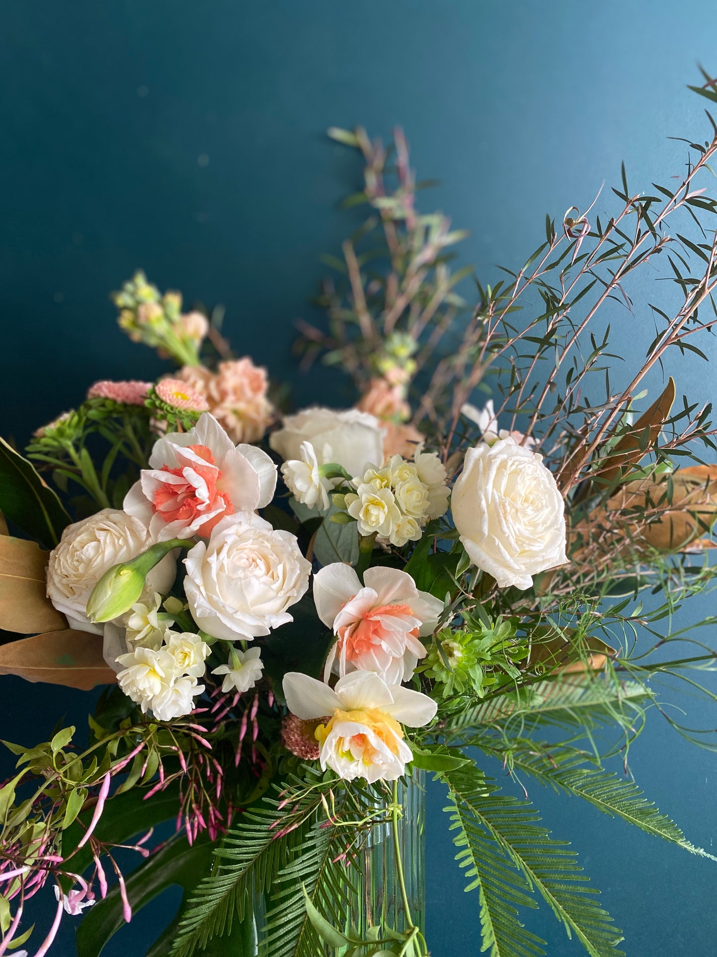 A small floral arrangement of white, pink and yellow flowers in a tall, glass vase