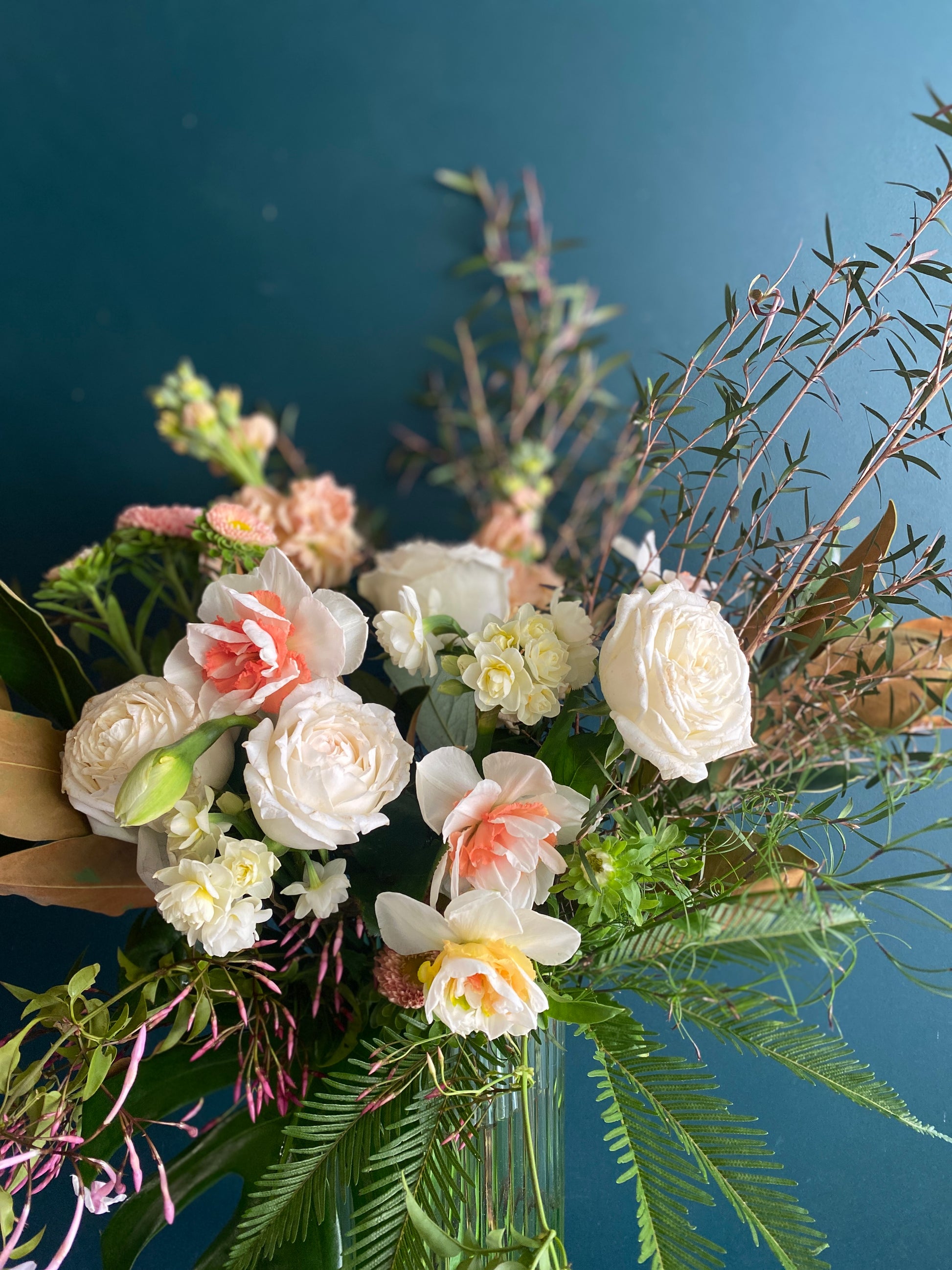 A small floral arrangement of white, pink and yellow flowers in a tall, glass vase