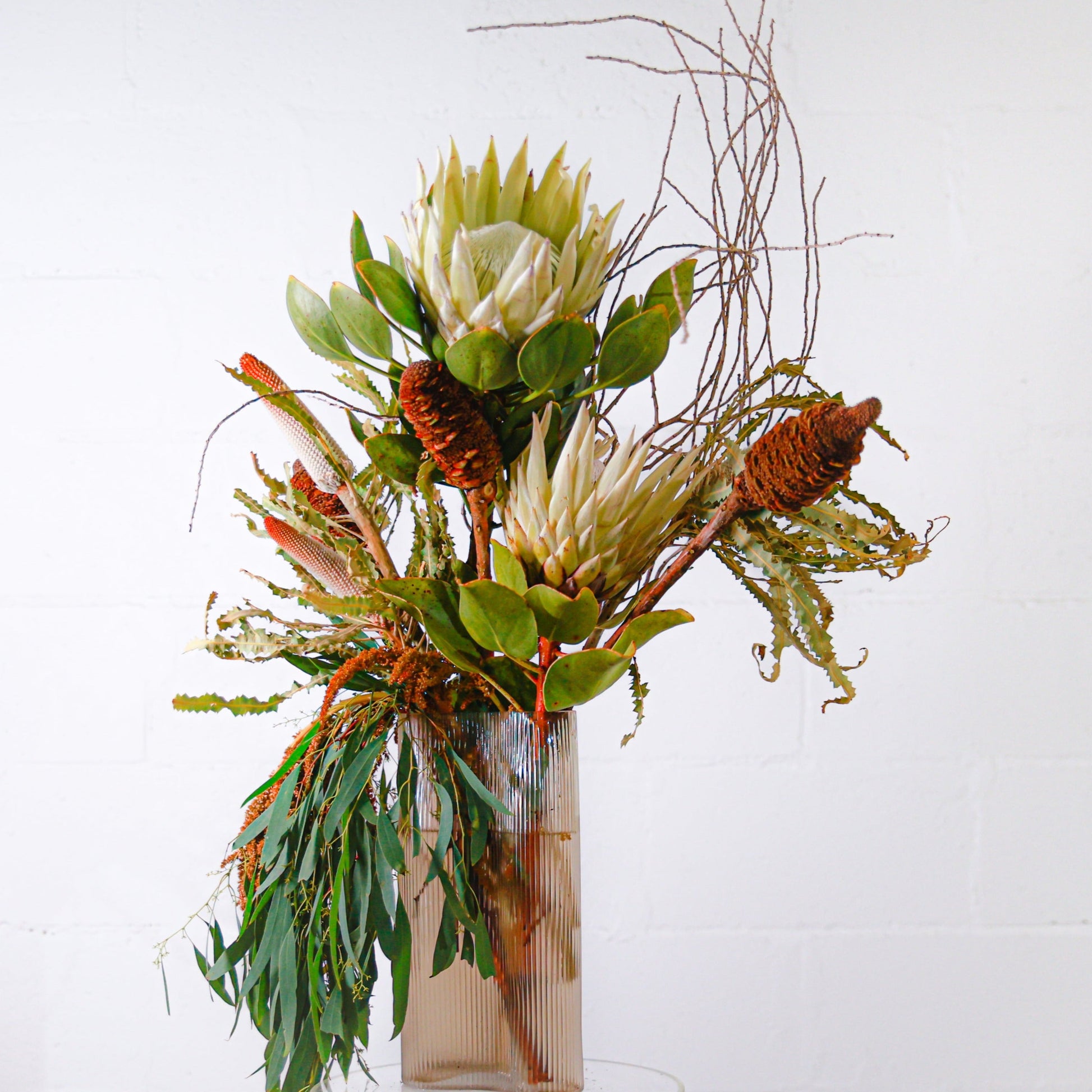 A neutral-coloured Native flower arrangement in white and natural tones for a corporate setting in an amber glass tall vase