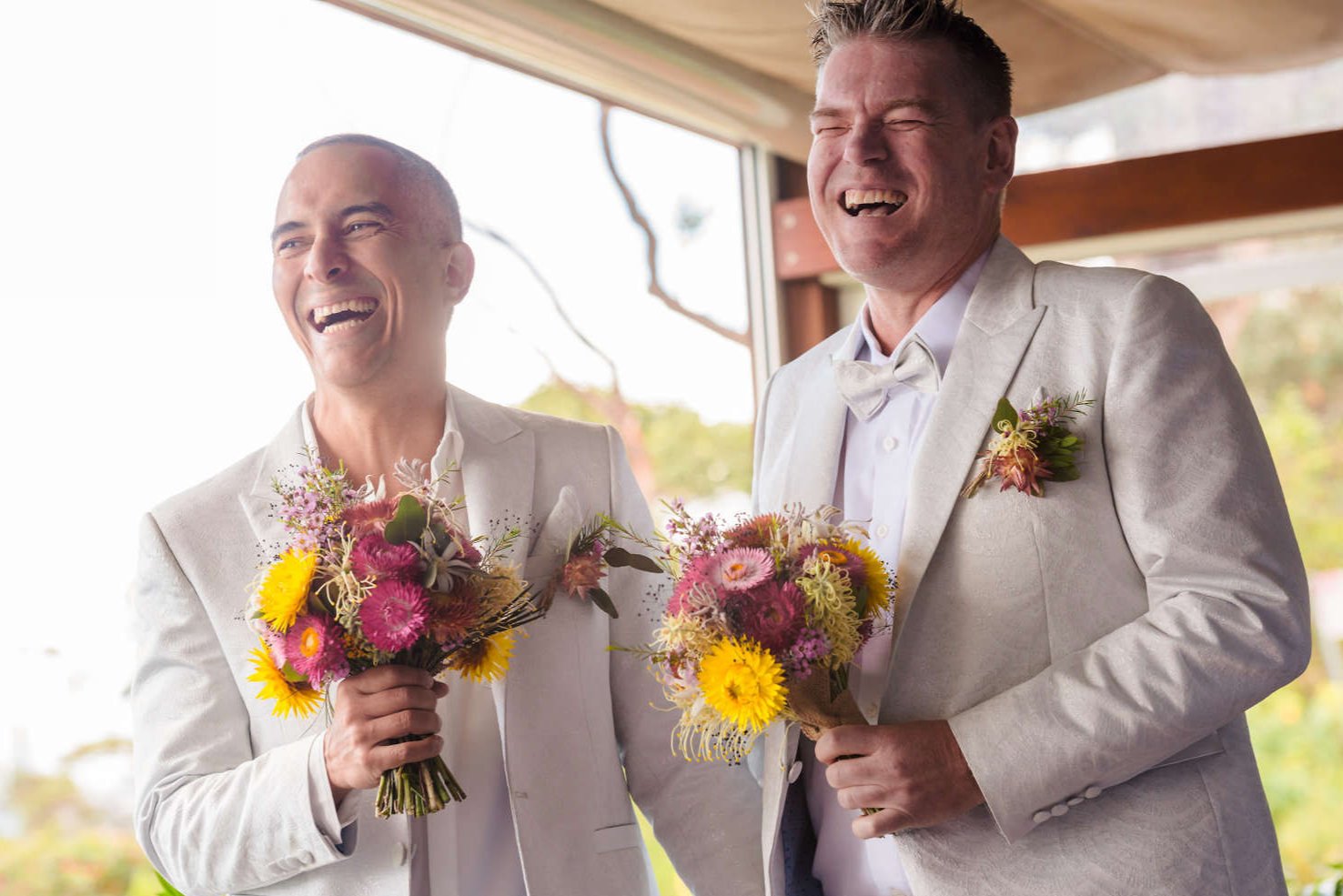 Two men celebrating their wedding, each holding a bright bouquet of Bold Botanicals wedding flowers