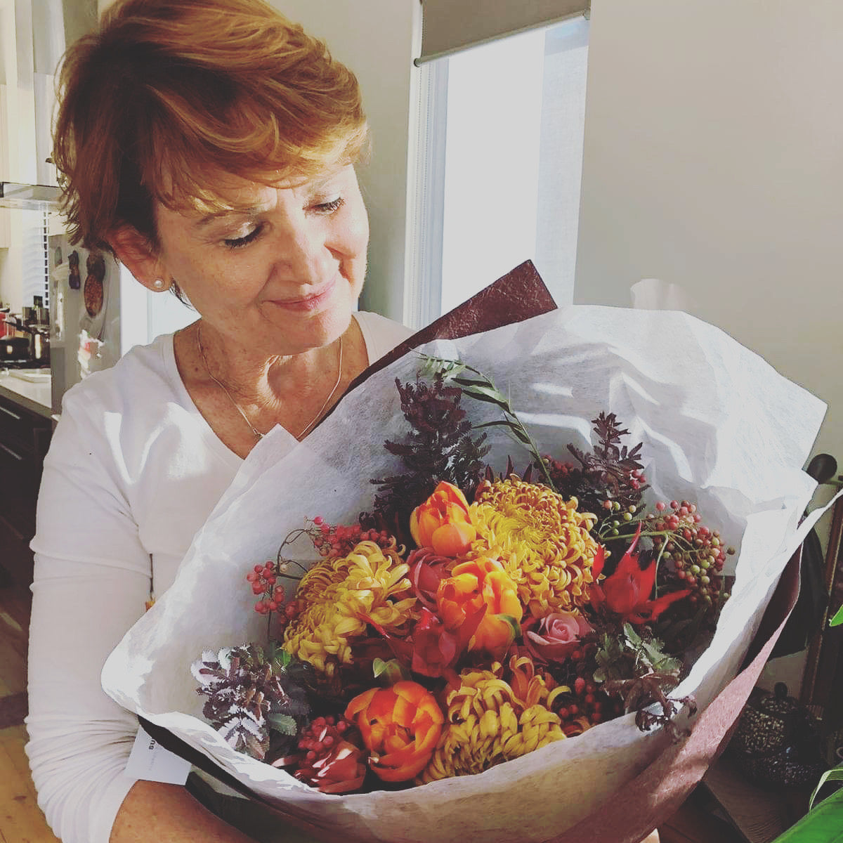 Mum holding and admiring her Autumn colour Mothers Day fresh flowers .