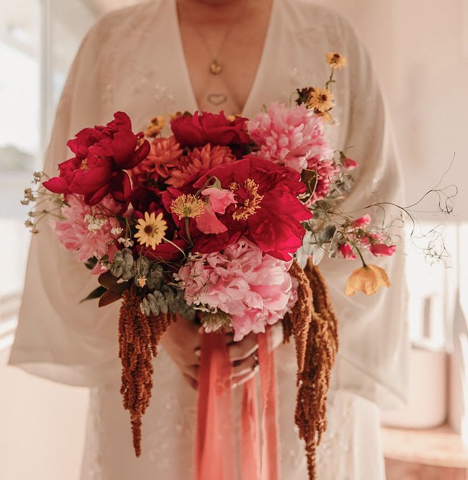 A bright wedding bouquet of red and pink flowers held by a bride