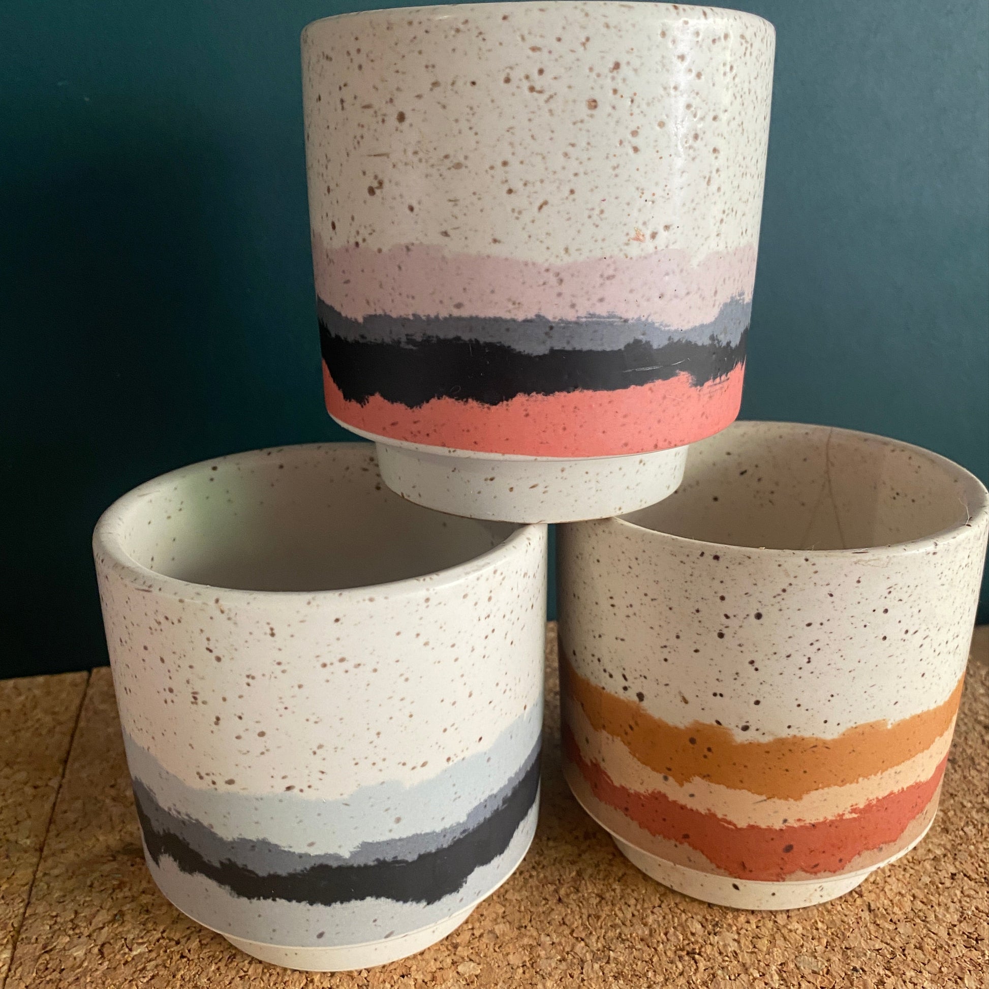 A stack of three glazed small succulent pots in bright colours and terrazzo look finish