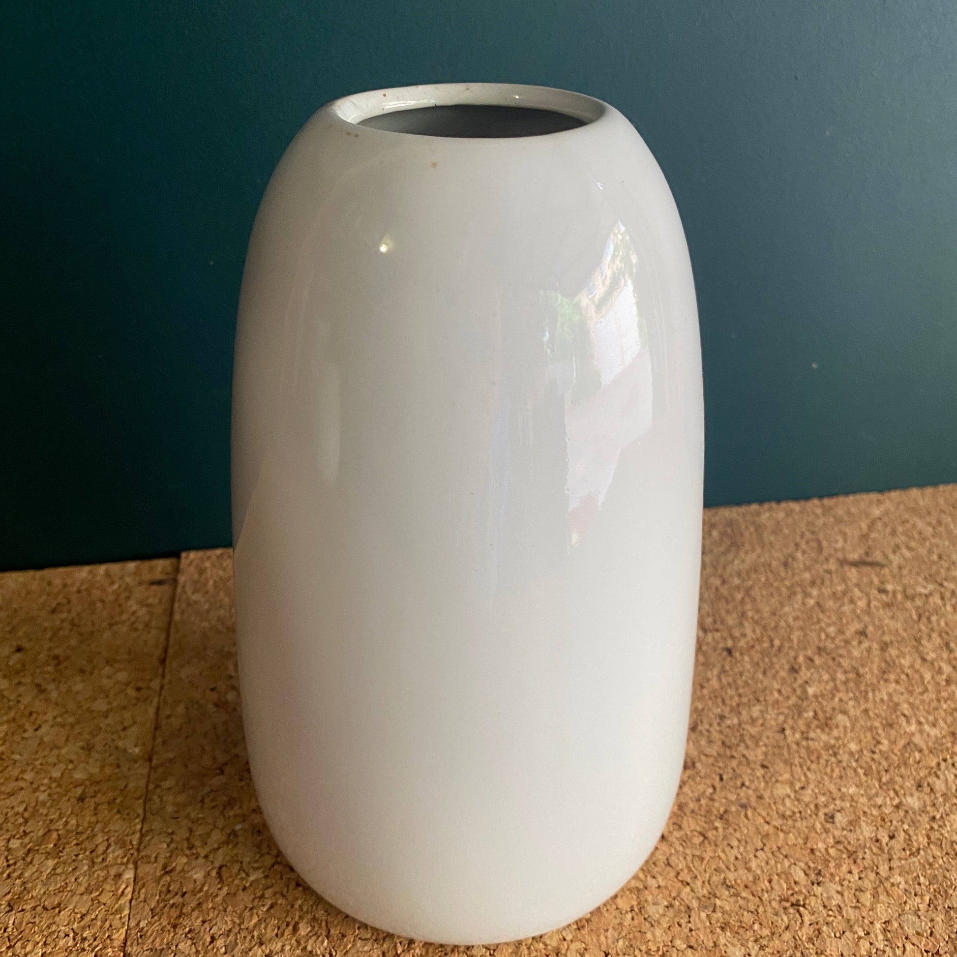 A tall white glossy finish ceramic vase with slight curve at top