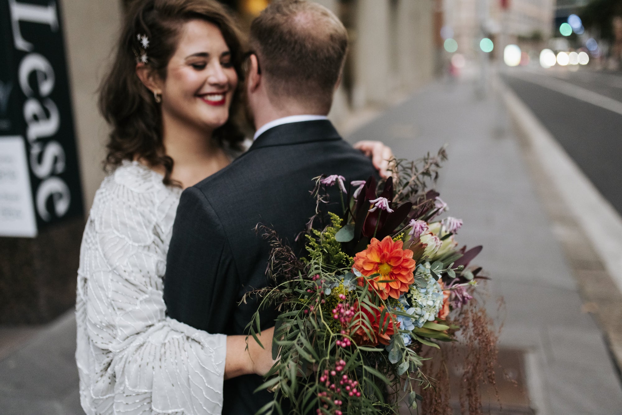 A smiling bride hugging her new husband, holding a bright wedding bouquet of flowers of Australian native flowers arranged by Bold Botanicals