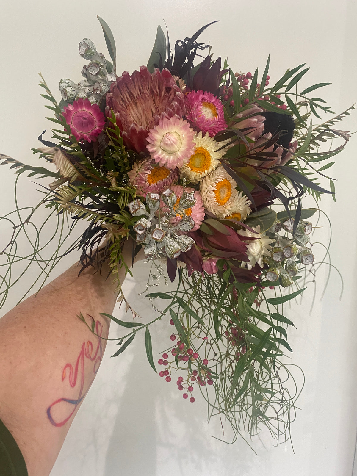 Bouquet of flowers held by a person with tattoos on a white background