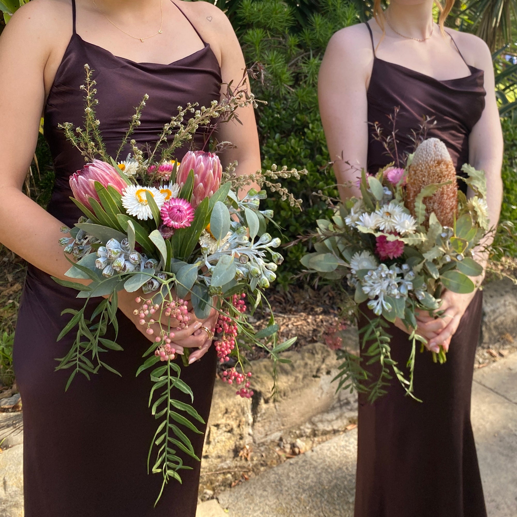 Two women holding native floral bouquets in brown silk dresses.